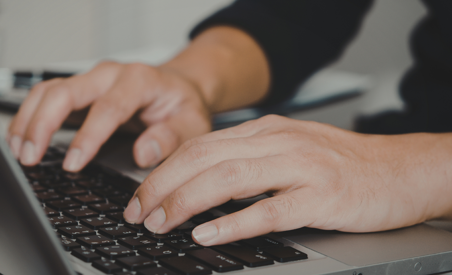 Close-up of a person’s hands typing on a laptop keyboard, with a blurred background.