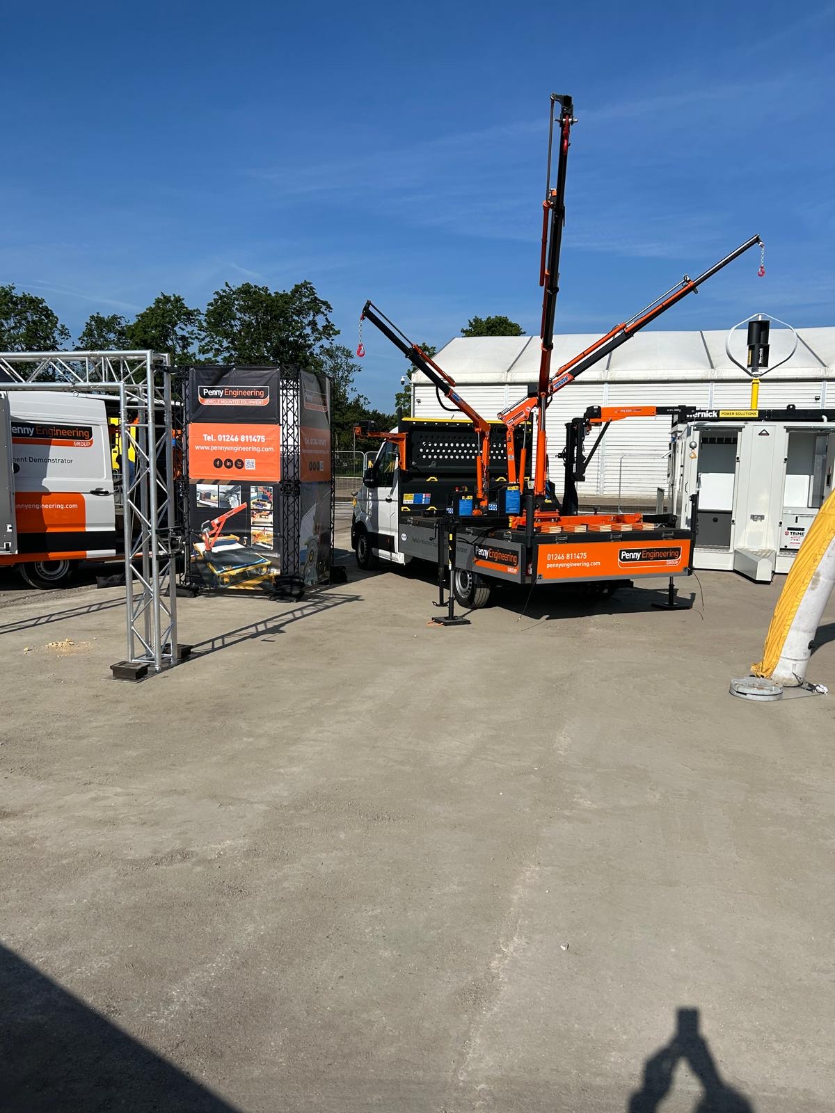 Construction site with lorries, equipment, and cranes from “Pfeifer Heavy Machinery.” Orange and white machinery is being used, with structures and a metal frame set up under a sunny blue sky.